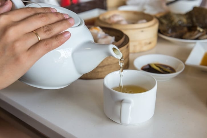 Pouring green tea from white teapot into a cup, dim sum etiquette and tips